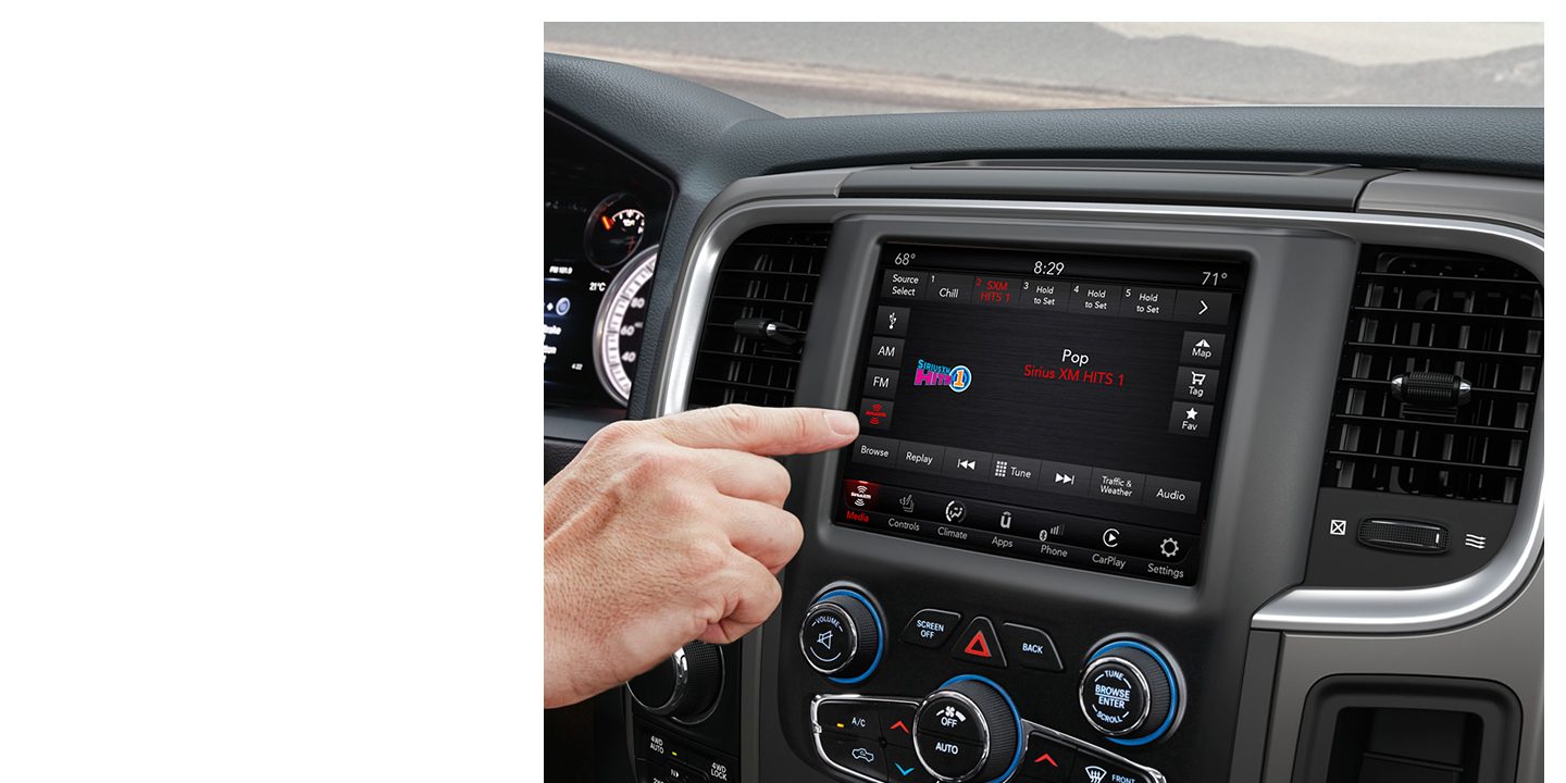 A close-up of the Uconnect touchscreen in a 2020 Ram 1500 Classic. A hand is pointing at the screen which is displaying SiriusXM information.