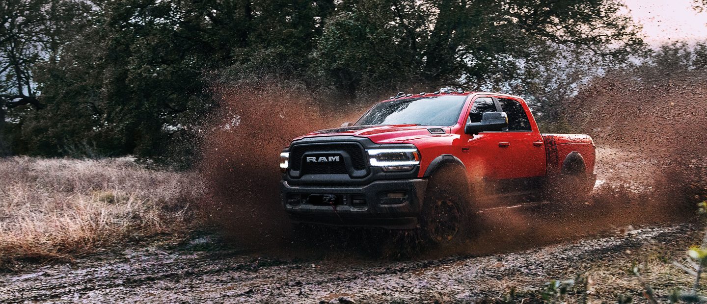 The 2022 Ram 2500 towing a flatbed with a digger on it through a muddy field.