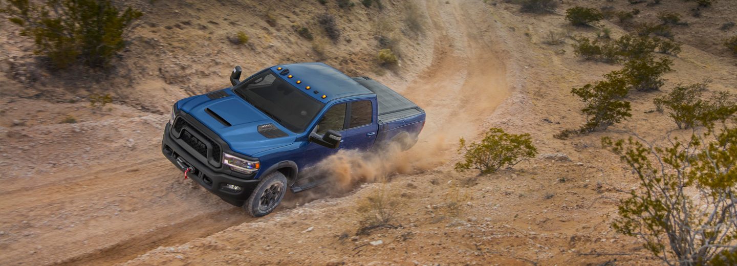 The 2022 Ram 2500 being driven on a dusty road lined with palm trees.