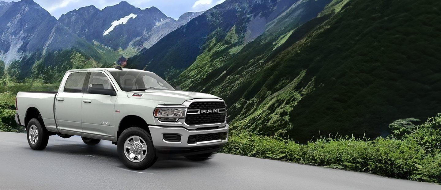 A 2023 Ram 3500 Limited Crew Cab towing a fifth wheel travel trailer as it is driven down a winding mountain road.