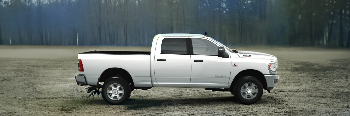 A 2023 Ram 3500 Laramie Crew Cab parked on a grassy field next to a barn with its doors open and a man and child standing in the doorway.