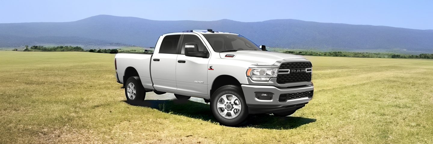 A 2023 Ram 3500 Limited Crew Cab with its headlamps on, being driven on a waterfront highway at dusk.