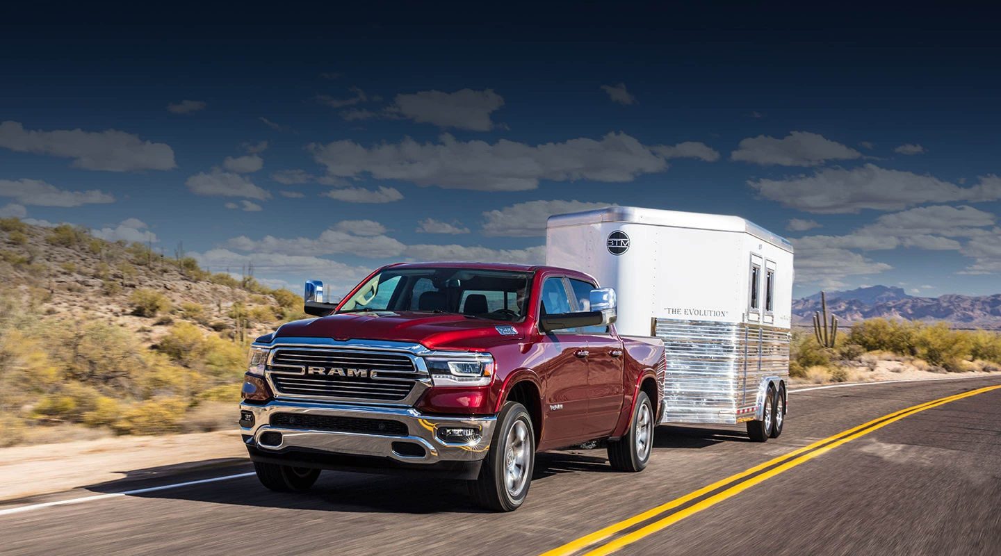 A 2020 Ram 1500 being driven on a road in the desert while towing a trailer.
