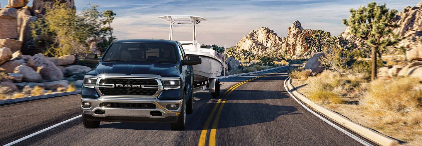 The 2023 Ram 1500 towing a motorboat on a winding road through rocky terrain.