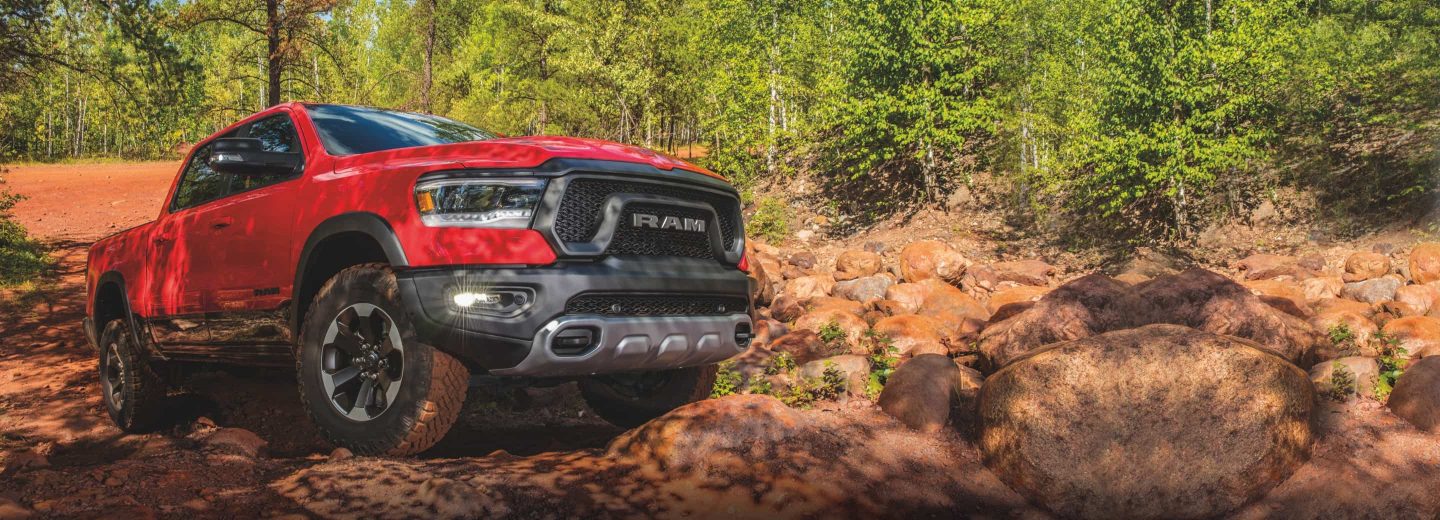 A red 2022 Ram 1500 Rebel 4x4 Crew Cab crawling over a steep rock formation in the woods.