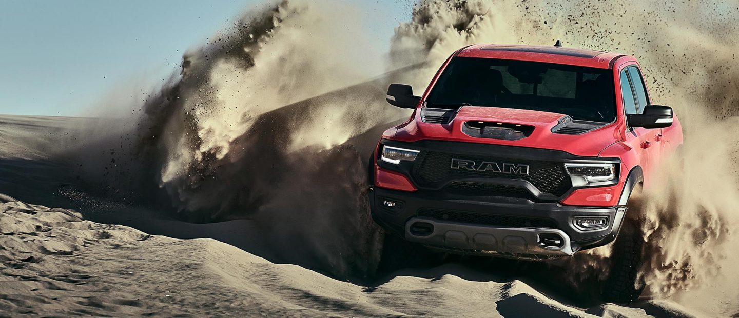 The 2022 Ram TRX surrounded by a large dust cloud as it's driven over a sand dune.