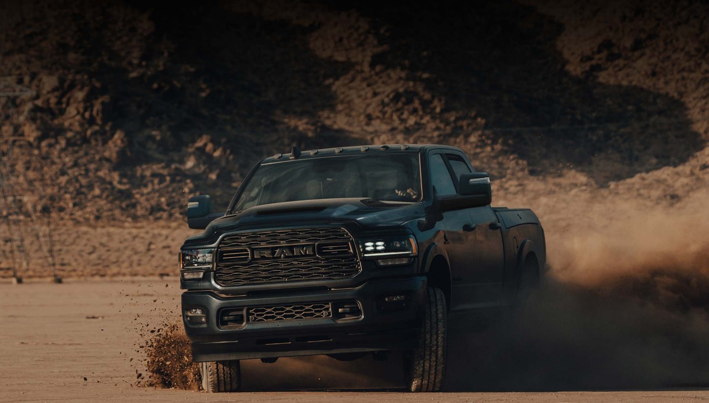 A 2023 Ram 2500 Limited Crew Cab being driven on a sandy clearing off-road, kicking up dust with its tires.