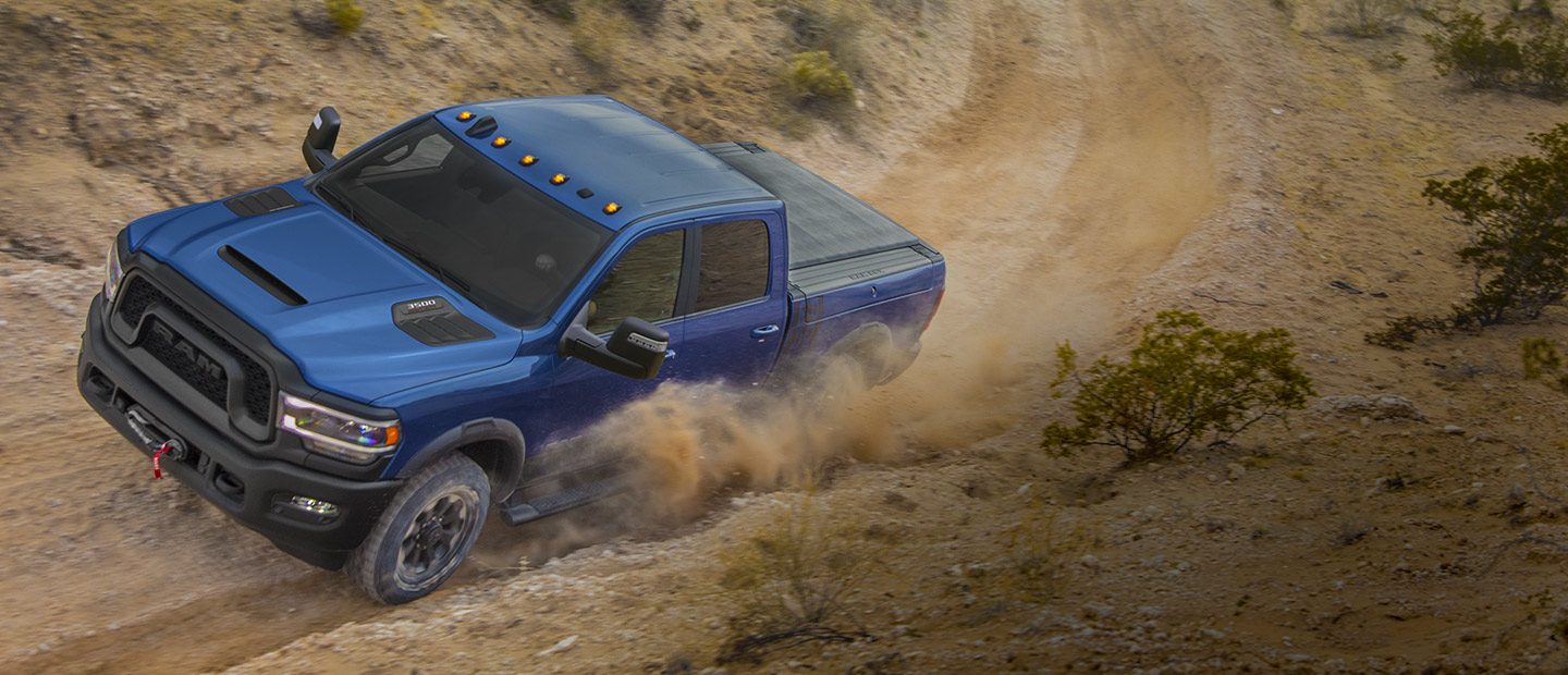 A blue 2023 Ram Power Wagon being driven on a dirt trail in the country.