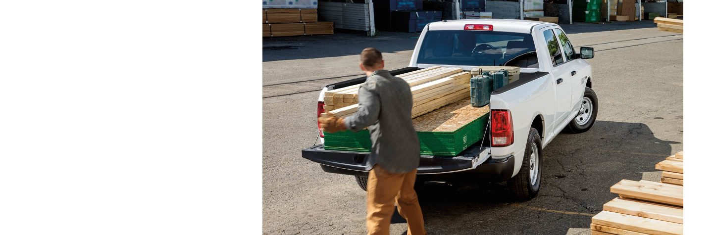 Un hombre carga madera en la plataforma de la camioneta de una Ram 1500 Tradesman 2023 4x4 Quad Cab.