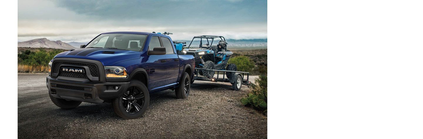 Una Ram 1500 Classic Warlock 2023 4x4 Crew Cab enganchada a un remolque de plataforma que transporta un ATV.