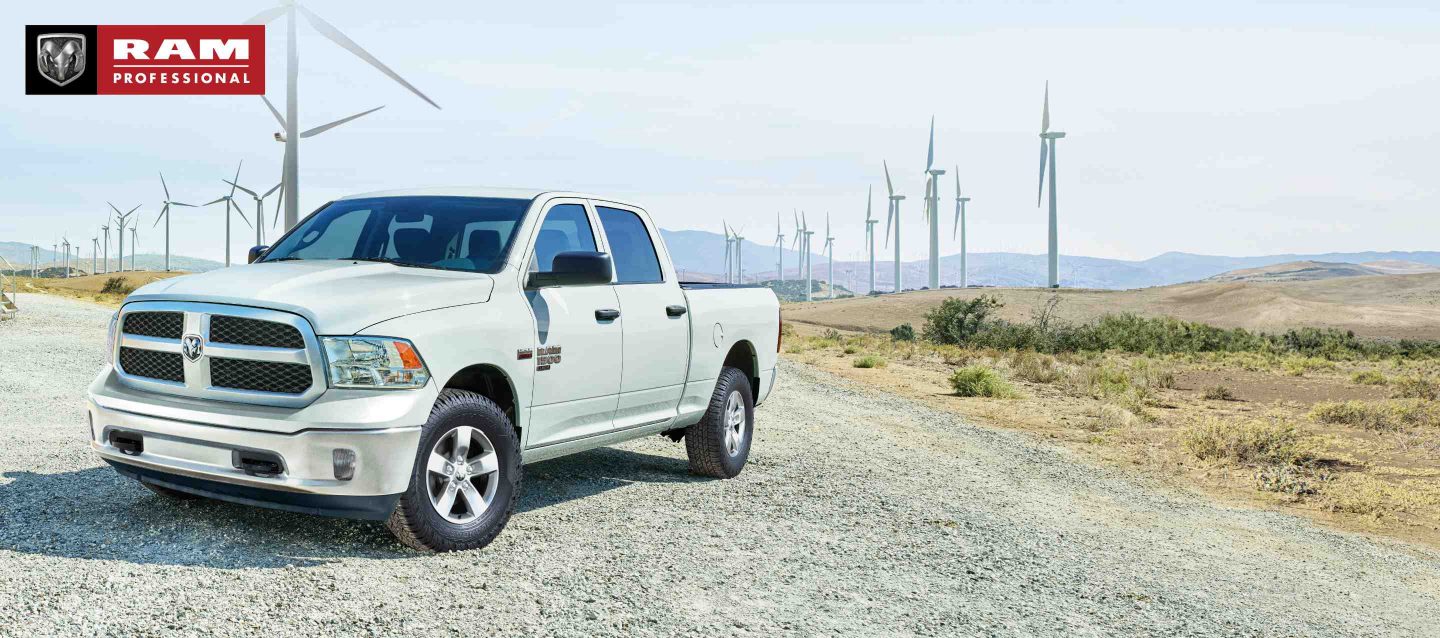 Una Ram 1500 Classic Tradesman Crew Cab 2023 blanca estacionada junto a un campo de molinos de viento. Ram profesional.