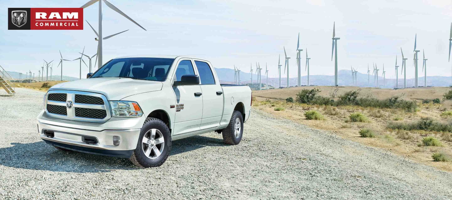 A white 2023 Ram 1500 Classic Tradesman Crew Cab parked beside a field of windmills. Ram Commercial Truck Season.