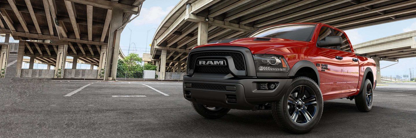 A red 2023 Ram 1500 Classic Warlock 4x4 Crew Cab parked under a freeway overpass.