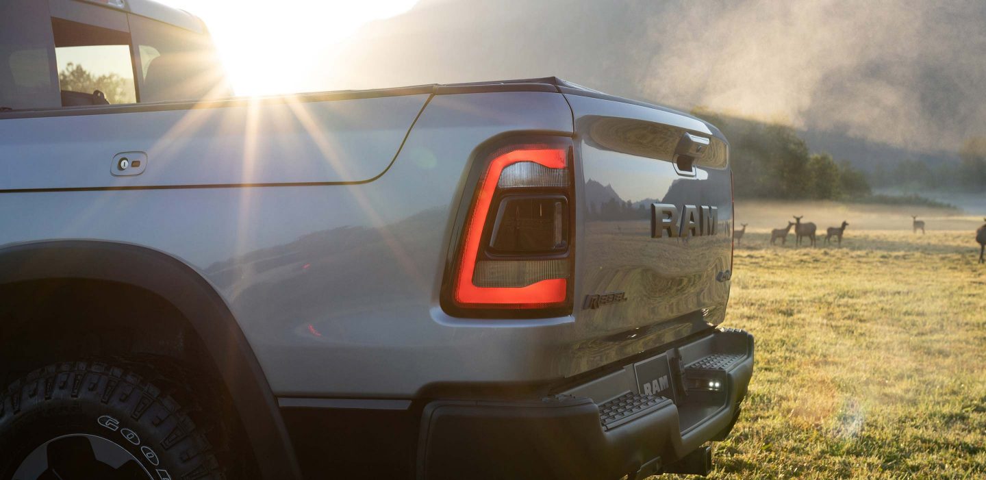 Display The 2023 Ram 1500 parked in a field at sunset with a herd of livestock in the distance.