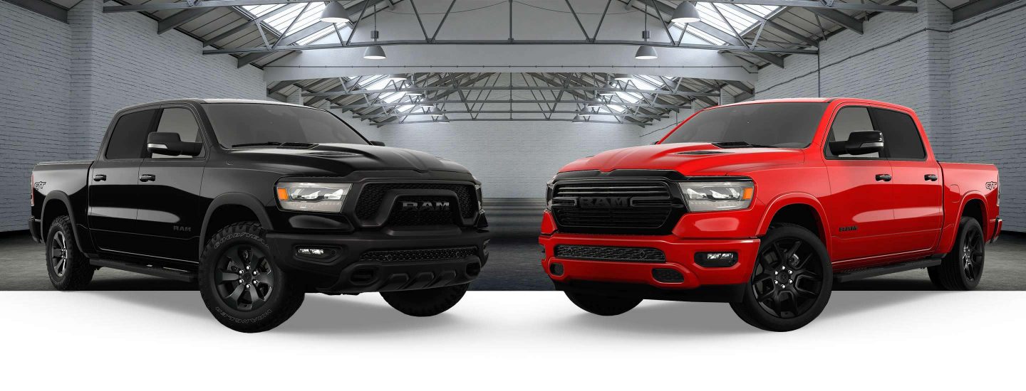 A black 2023 Ram 1500 Rebel G/T Crew Cab and a red 2023 Ram 1500 Laramie G/T Crew Cab with the backdrop of a large exhibition space.
