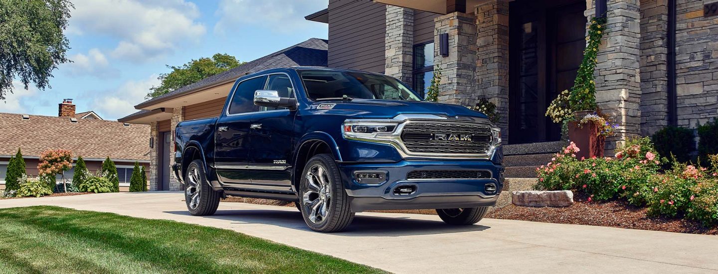 A blue 2023 Ram 1500 Limited Elite parked in the driveway of a large brick home.