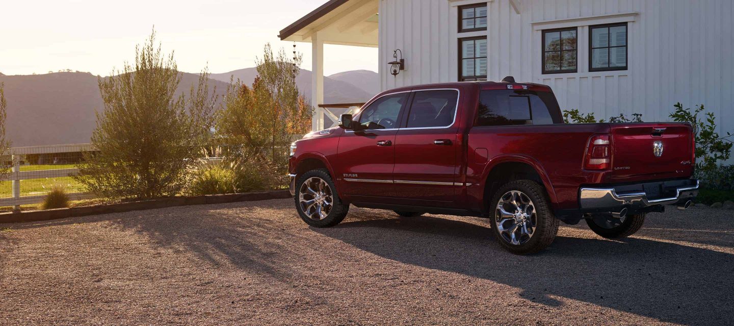 The 2023 Ram 1500 parked on a gravel driveway beside a farmhouse.