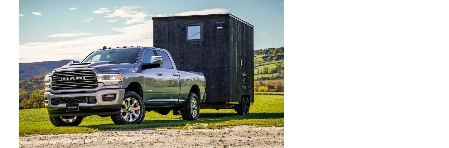 Una Ram 2500 Laramie Crew Cab remolcando un pequeño remolque por un camino rural.