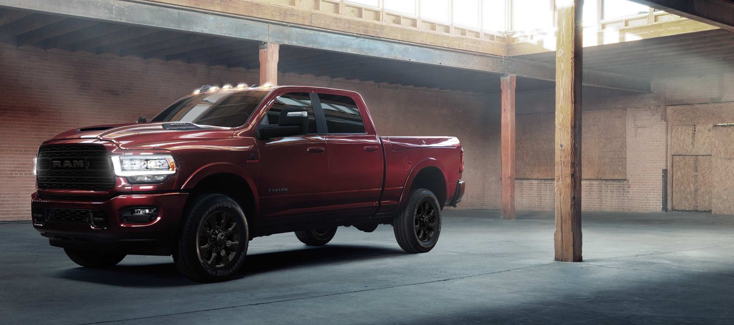 An angled profile of a red 2023 Ram 2500 Limited parked in a commercial garage with its headlamps on.