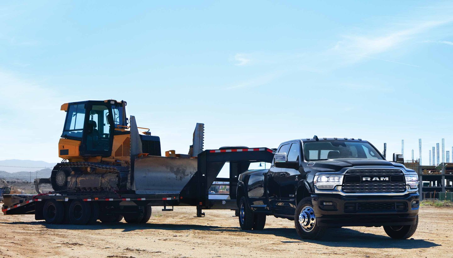 A 2023 Ram 3500 Limited Crew Cab towing a fifth wheel flatbed trailer with an excavator on it.