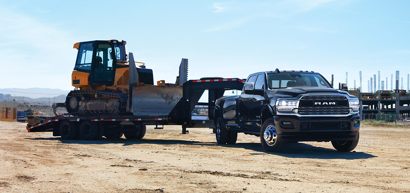 A 2023 Ram 3500 Limited Crew Cab towing a fifth wheel flatbed trailer with an excavator on it.