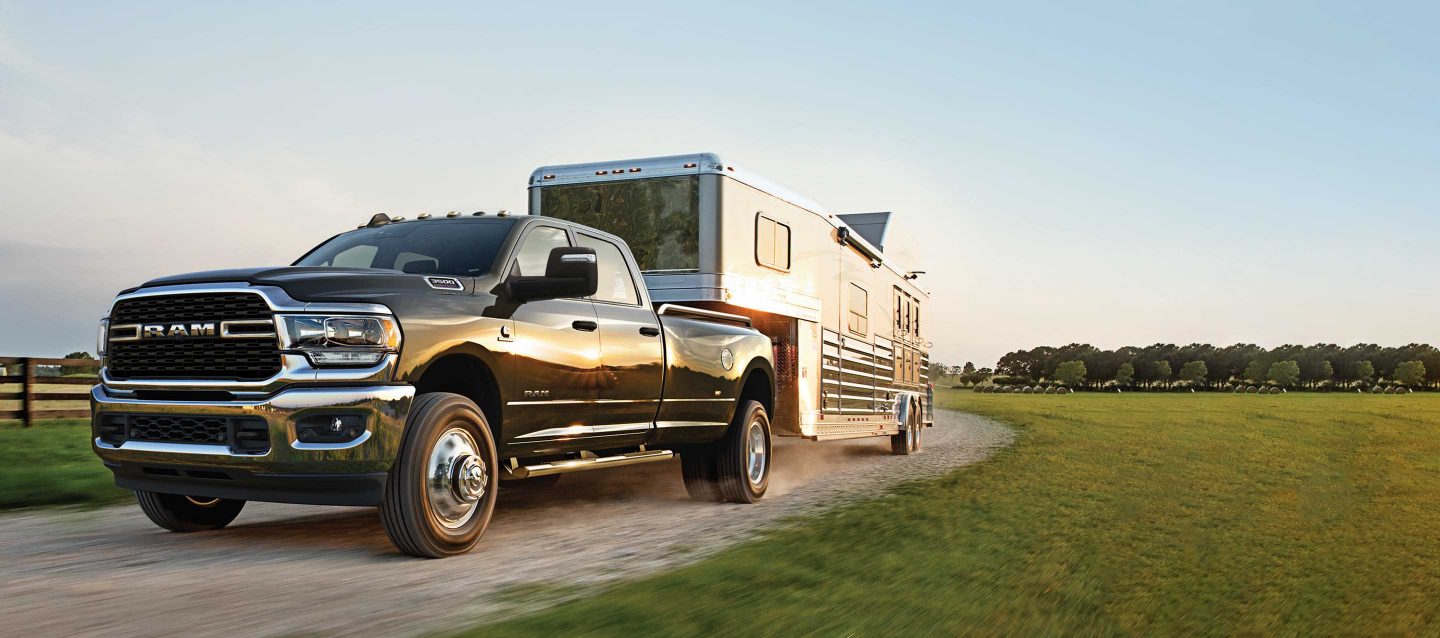 An angled profile of a 2023 Ram 3500 Big Horn Crew Cab towing a fifth wheel travel trailer.