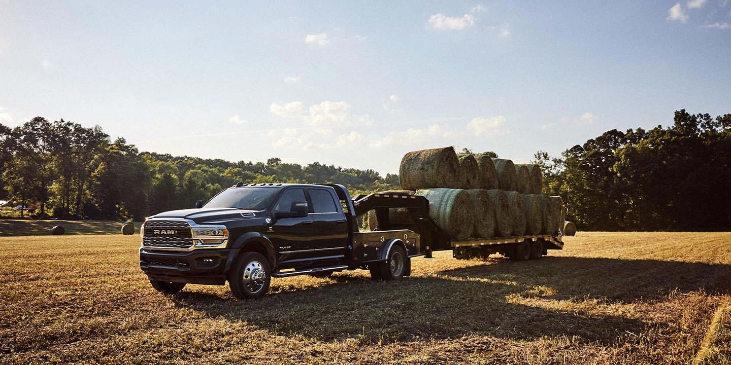 Una Ram Chassis Cab 2023 circulando por un campo abierto con un remolque tipo cuello de cisne lleno de fardos de heno.