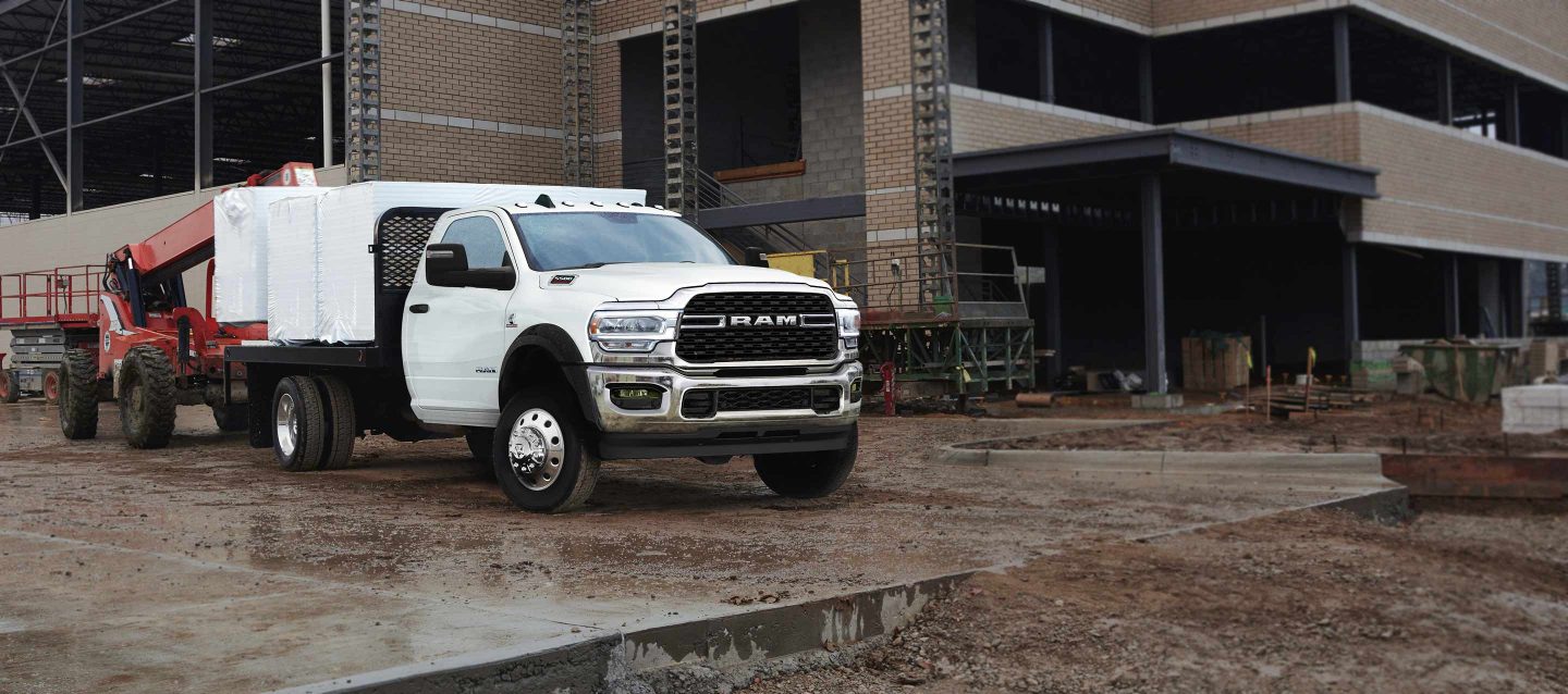 A 2023 Ram Chassis Cab with a platform upfit loaded with building materials, parked at a commercial construction site.