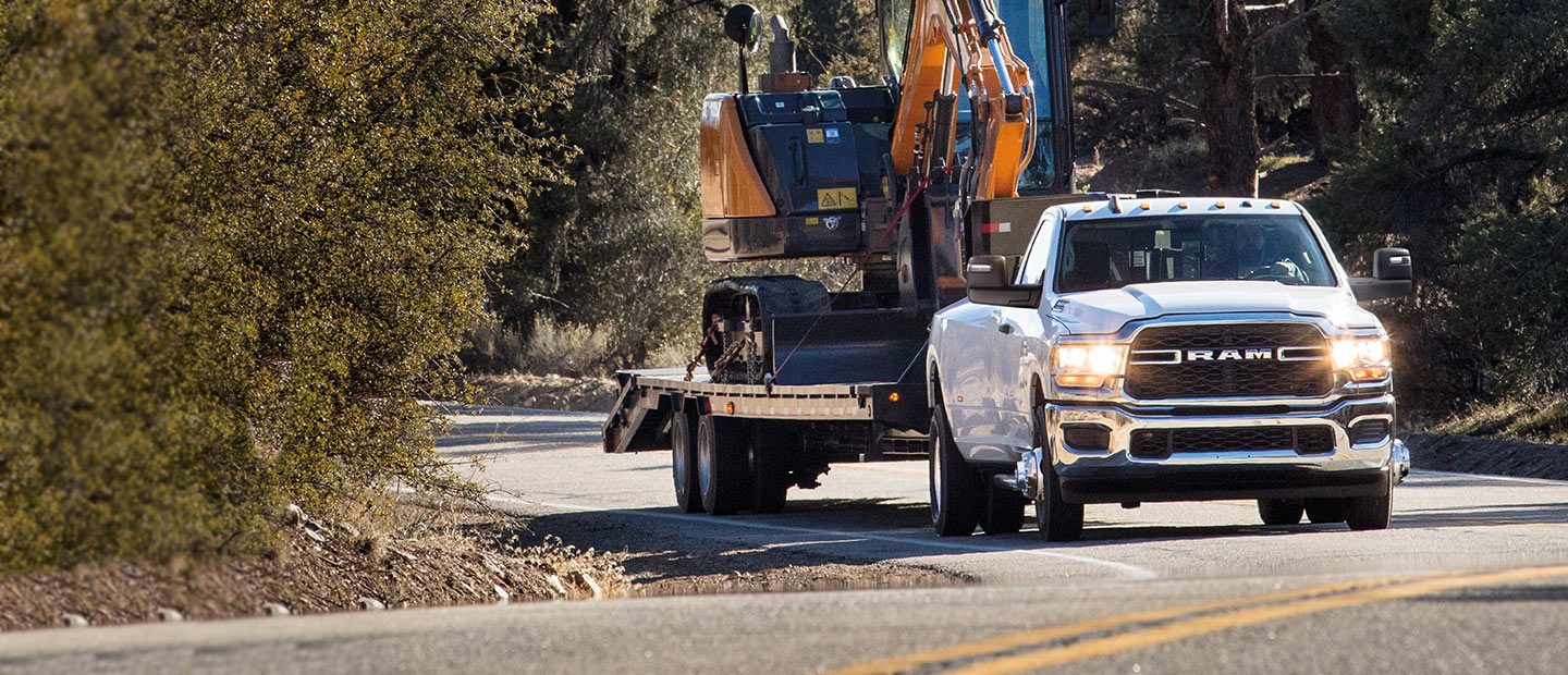 Una Ram 3500 Tradesman 2023 blanca circulando por una carretera, acarreando una grúa móvil en un remolque.