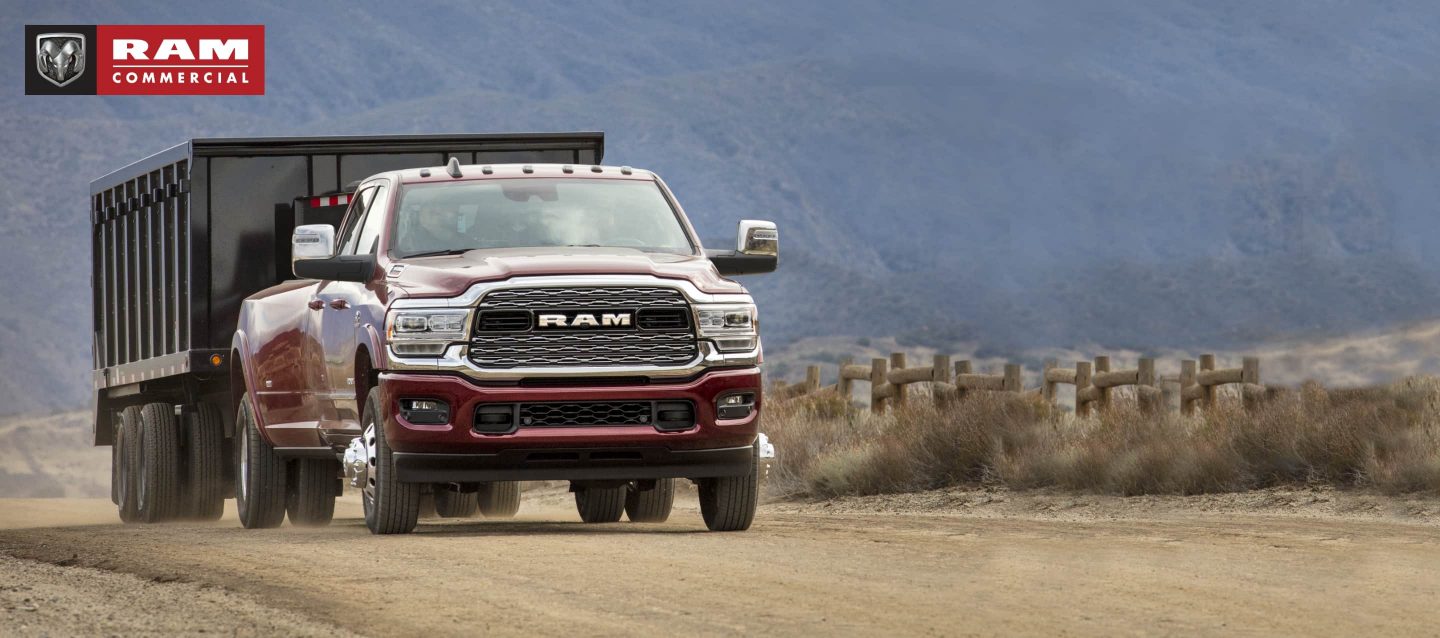 A 2023 Ram 3500 Limited towing a dump body trailer on a dirt road with mountains in the distance.