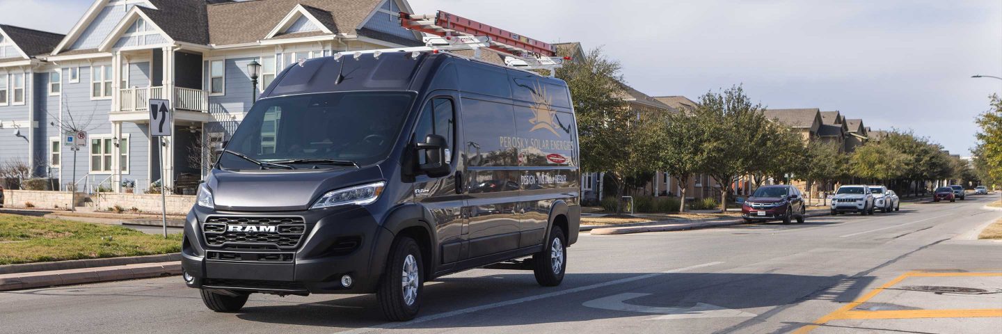 Una Ram ProMaster 2500 Cargo Van High Roof 2023 estacionada en un barrio residencial, con una escalera enganchada en la parrilla portaequipajes.