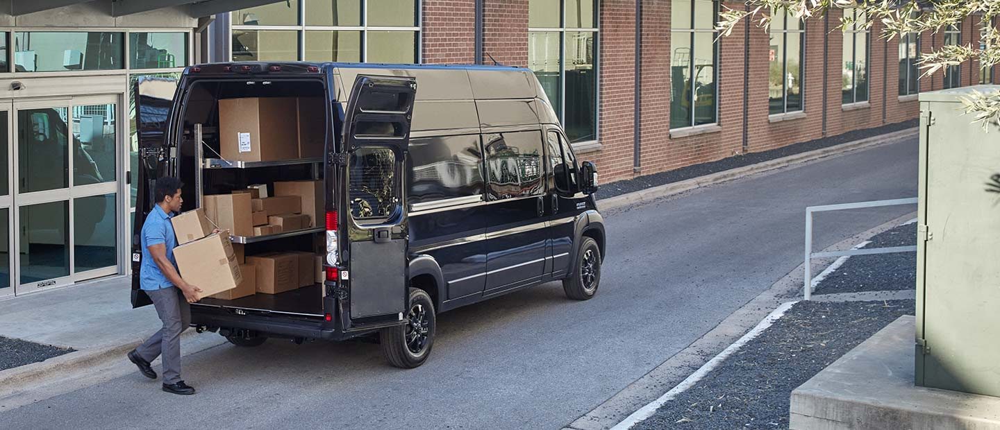 Un hombre cargando cajas a través de las puertas traseras abiertas de una Cargo Van Ram ProMaster 3500 2023 mejorada con estantes.