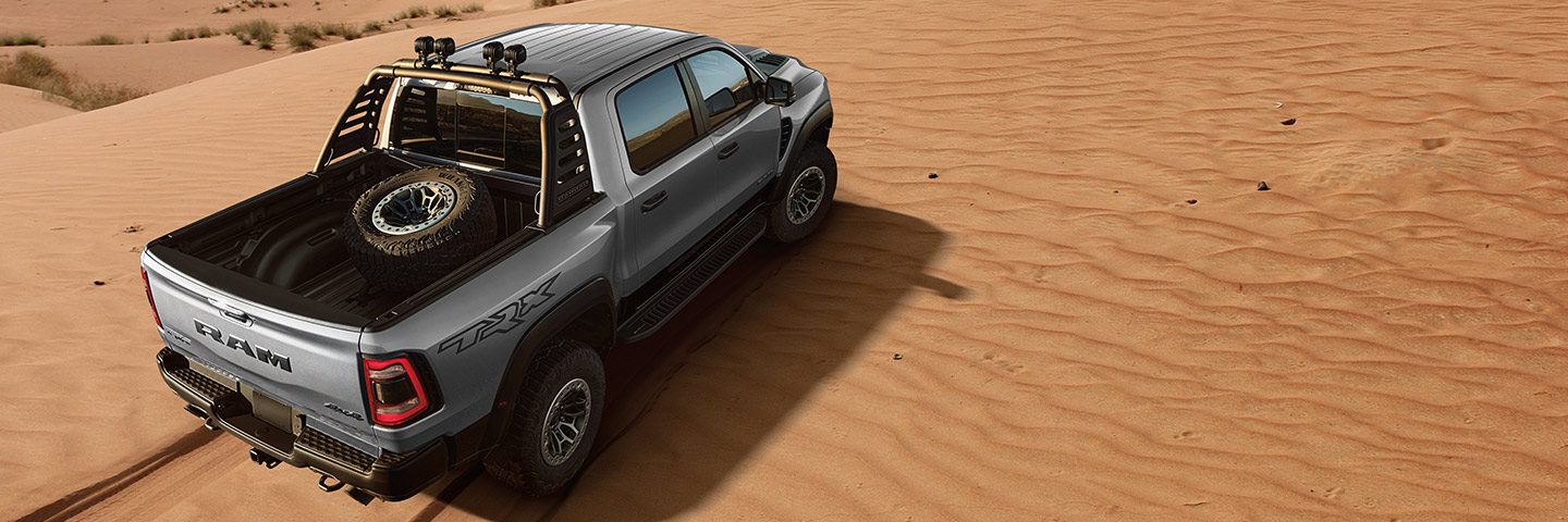 The 2023 Ram 1500 TRX being driven off-road on sand with a full-size spare tire mounted in the truck bed.