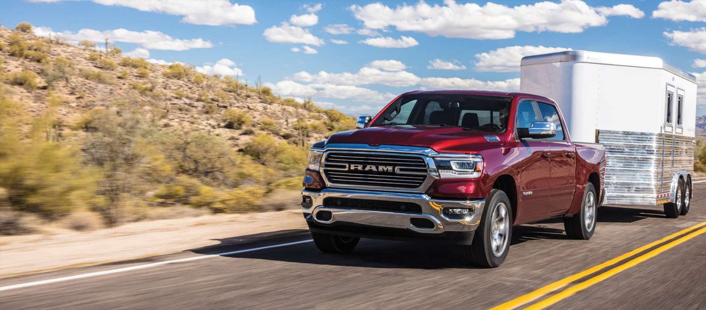 Una Ram 1500 Laramie Crew Cab 2024 roja remolcando un remolque de caballo mientras circula por una carretera en el desierto.