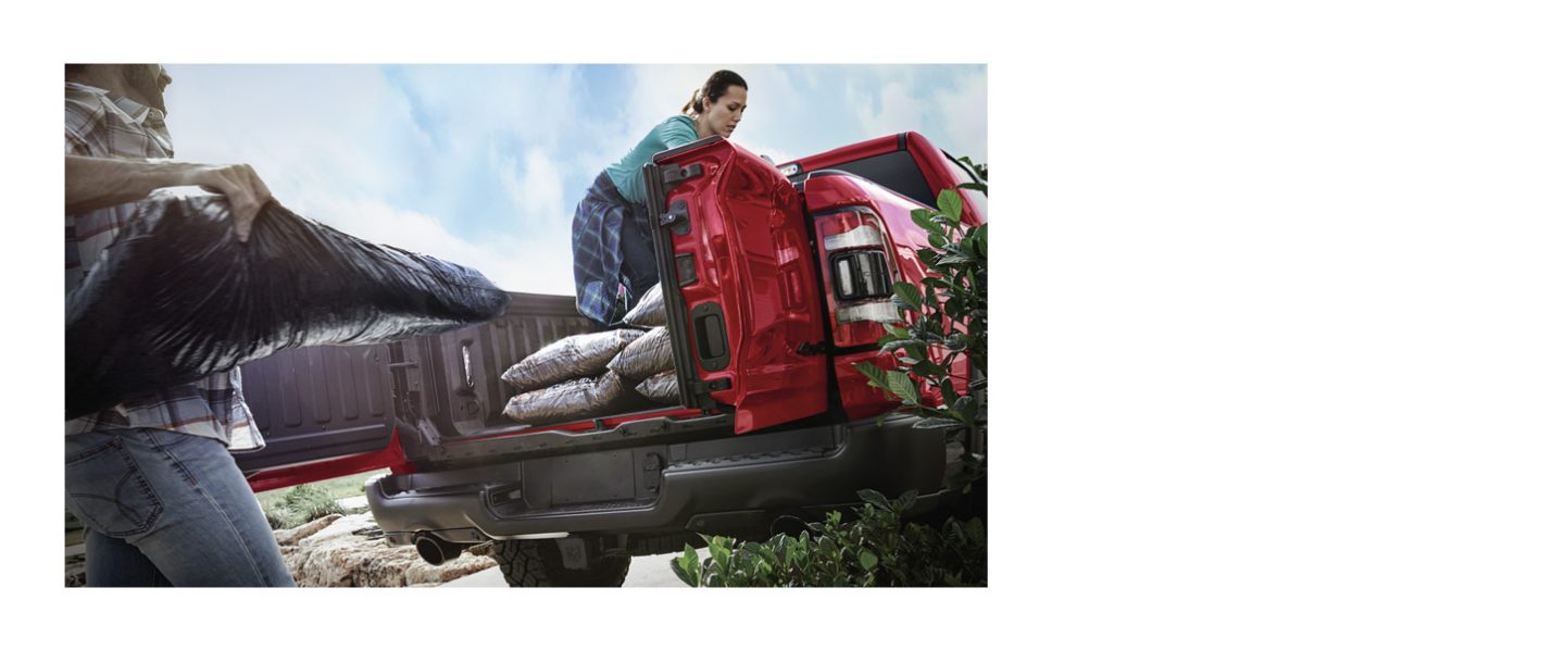 La plataforma de carga en una Ram 1500 2024 roja con sus puertas abatibles abiertas mientras se carga con materiales de jardinería.