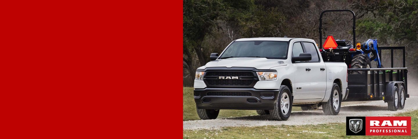 Una Ram 1500 Tradesman Crew Cab 2024 blanca remolcando un tractor en un remolque. Ram profesional.