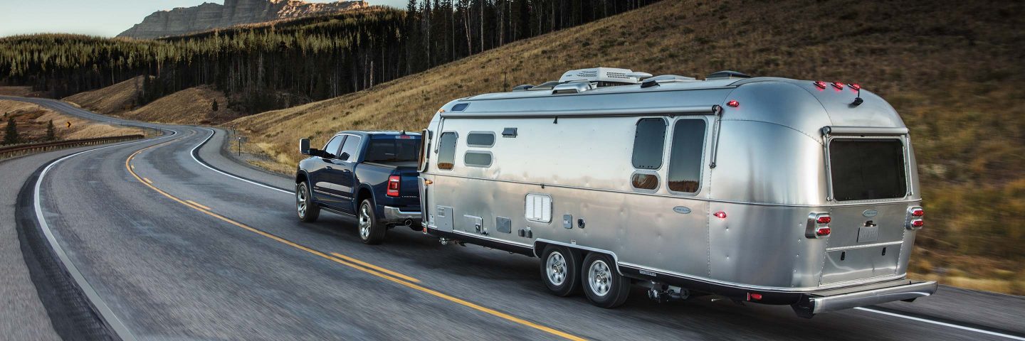 Una Ram 1500 Limited Crew Cab 2024 negra remolcando un gran tráiler de viaje mientras circula por una carretera sinuosa a través de las montañas.