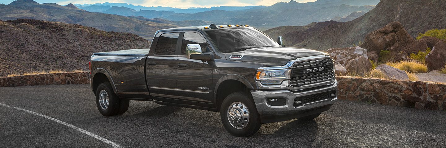 La Ram 3500 limited crew cab gris 2024 aparcado en el sitio de la autopista con vistas a un vasto conjunto de montañas.