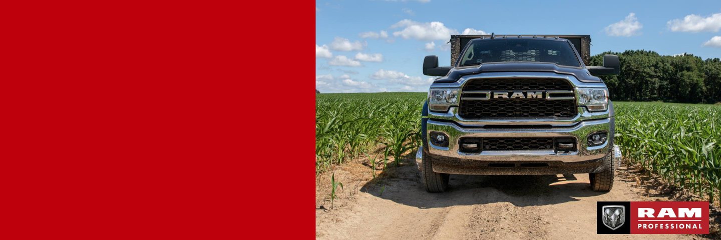 Ángulo frontal de una Ram 4500 Tradesman Chassis Cab 2024 con una mejora de plataforma de estacas en un camino de tierra, entre campos de cultivos. Ram profesional.