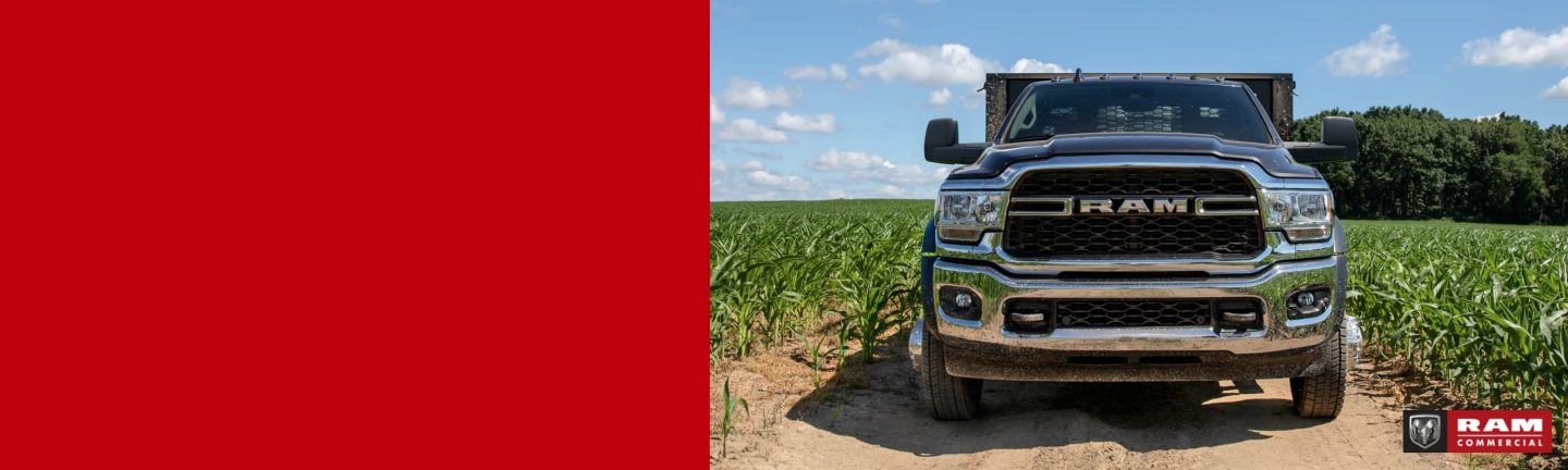 A head-on angle of a 2024 Ram 4500 Tradesman Chassis Cab with a stake bed upfit on a dirt road between fields of crops. Ram Commercial.