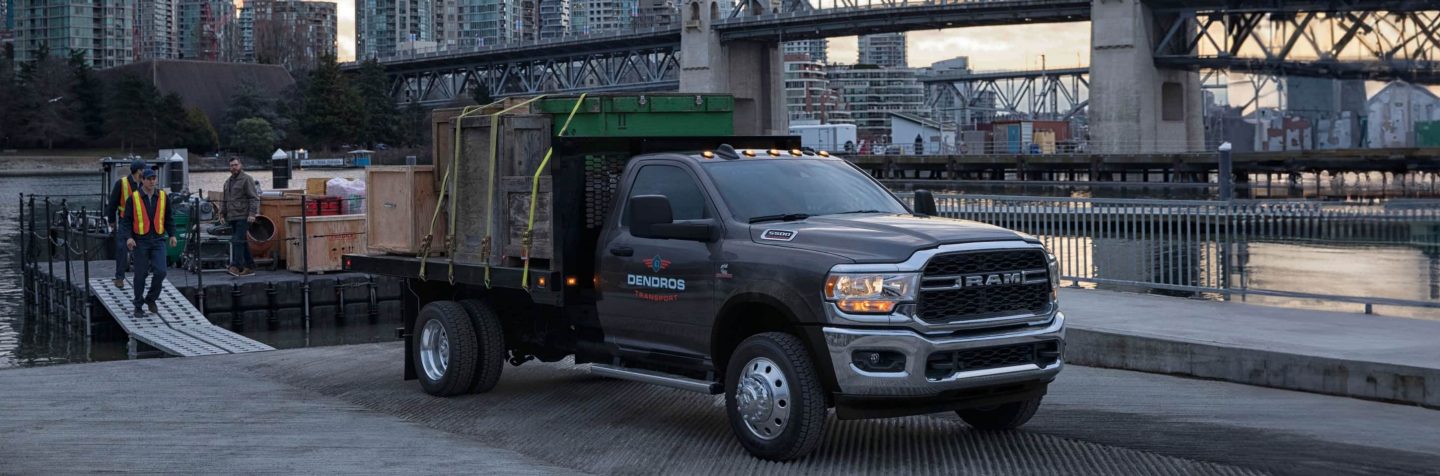 Una Ram 5500 Tradesman Chassis Cab Regular Cab 2024 estacionada en un muelle de río, cargada con cajas de madera.