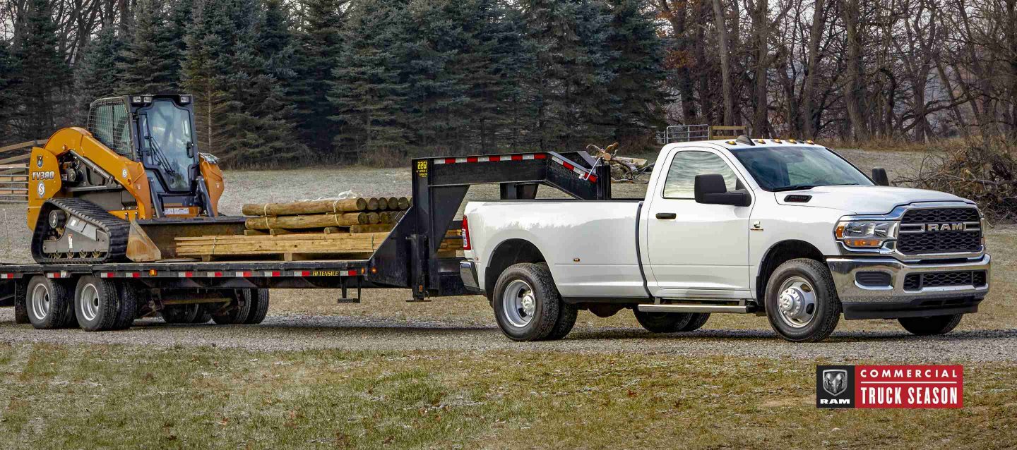 Ақ түсті 2024 Ram 3500 Tradesman 4x4 Regular Cab экскаватор мен ағаш тиелген бесінші доңғалақты жалпақ тіркемені сүйреп апарып жатыр.