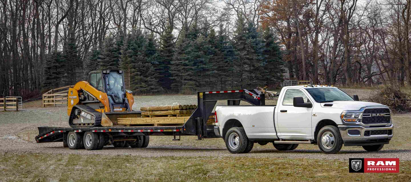 Una Ram 3500 Tradesman 4x4 Regular Cab 2024 blanca llevando un remolque de plataforma de quinta rueda cargado con una excavadora y madera. Ram Professional.