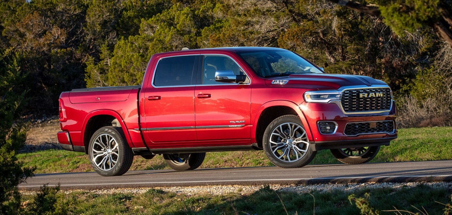 A blue 2026 Ram 1500 Rebel 4x4 Crew Cab climbing a rocky trail off-road, with a forest in the background.