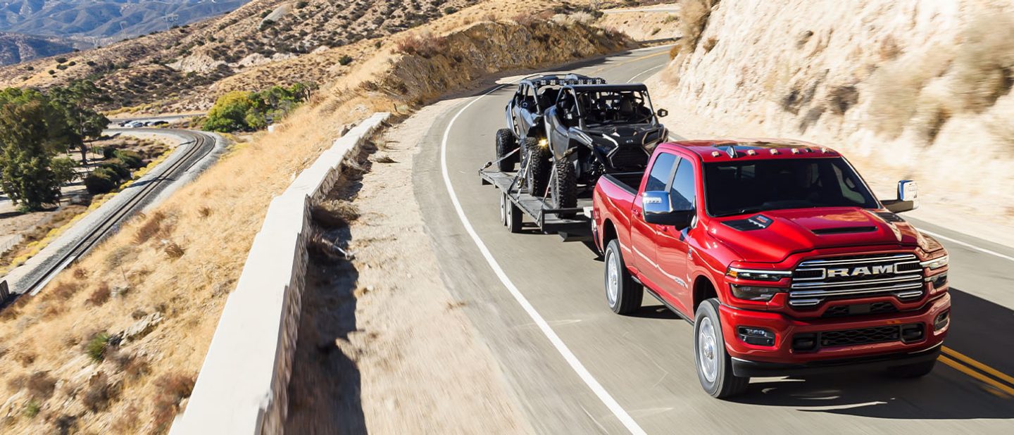 Una Ram 2500 Laramie 4x4 Crew Cab 2025 roja circulando por una carretera en las montañas, mientras remolca dos ATV.