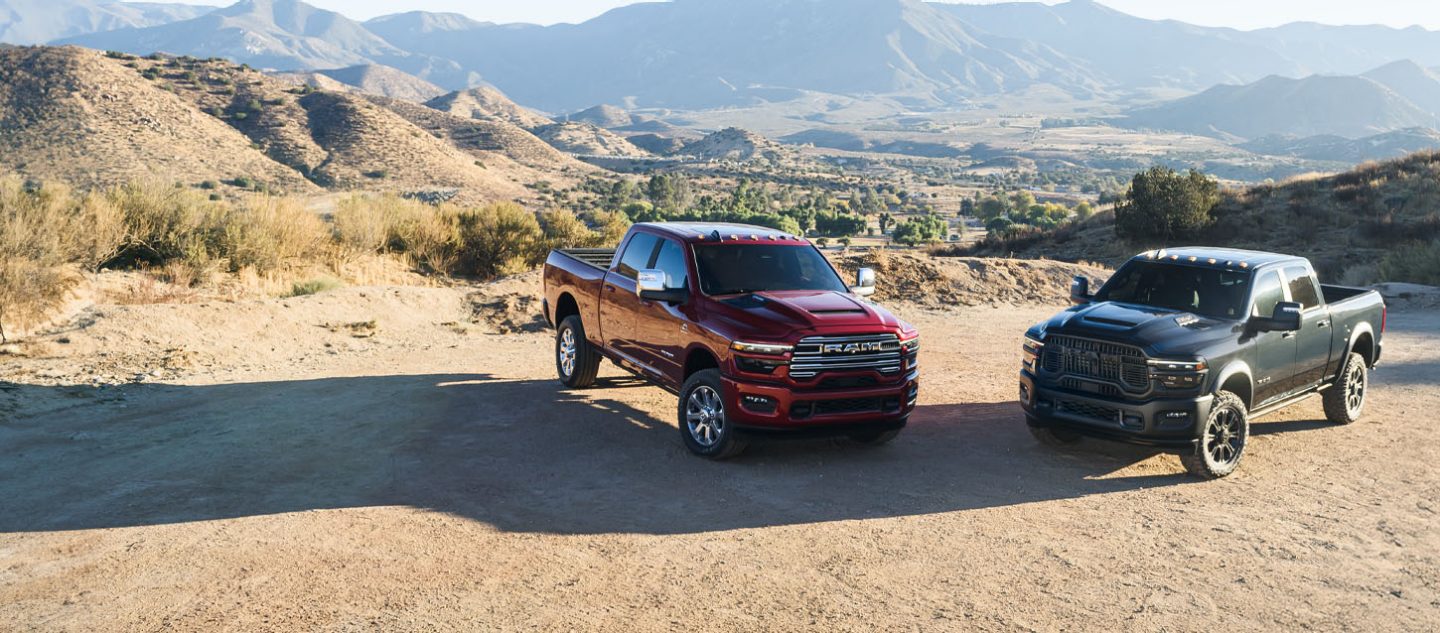 Una Ram 2500 Laramie 4x4 Crew Cab 2025 roja y una Ram 2500 Rebel 4x4 Crew Cab negra estacionadas en un claro, en las montañas.