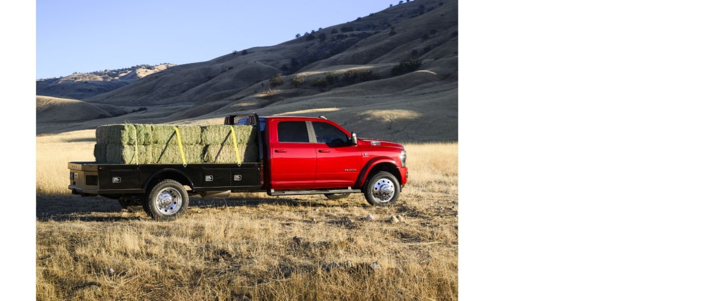 Vista lateral del lado del pasajero de una Ram 5500 Laramie Chassis Crew Cab 2025 en un campo transportando grandes fardos de heno sobre su plataforma larga mejorada.