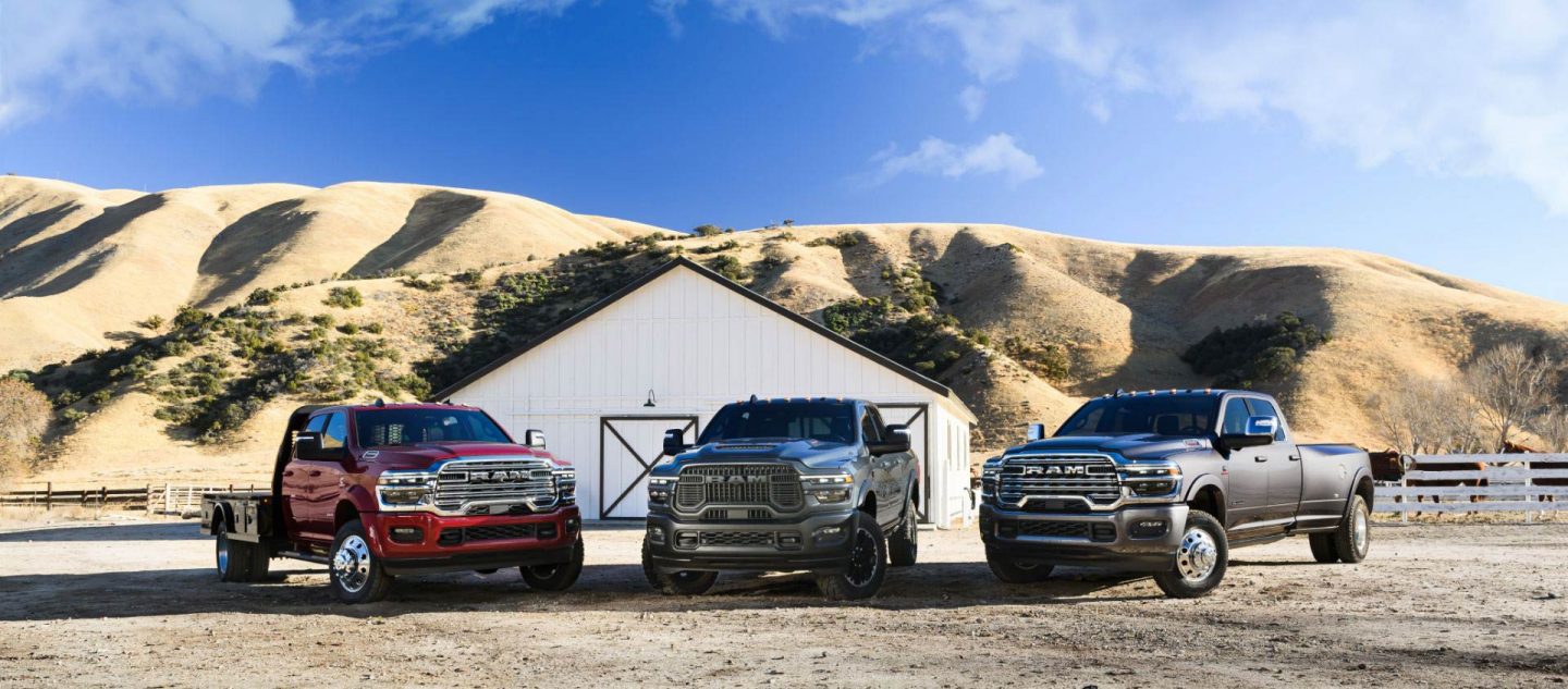 Tres camionetas Ram estacionadas en un rancho. De izquierda a derecha: una Ram 5500 Laramie Chassis Crew Cab 2025 roja, una Ram 2500 Rebel Crew Cab 2025 azul y una Ram 3500 Limited Longhorn Crew Cab 2025 gris.