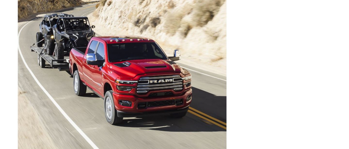Una Ram 2500 Laramie 4x4 Crew Cab 2025 roja circulando por una carretera en las montañas, mientras remolca dos ATV.
