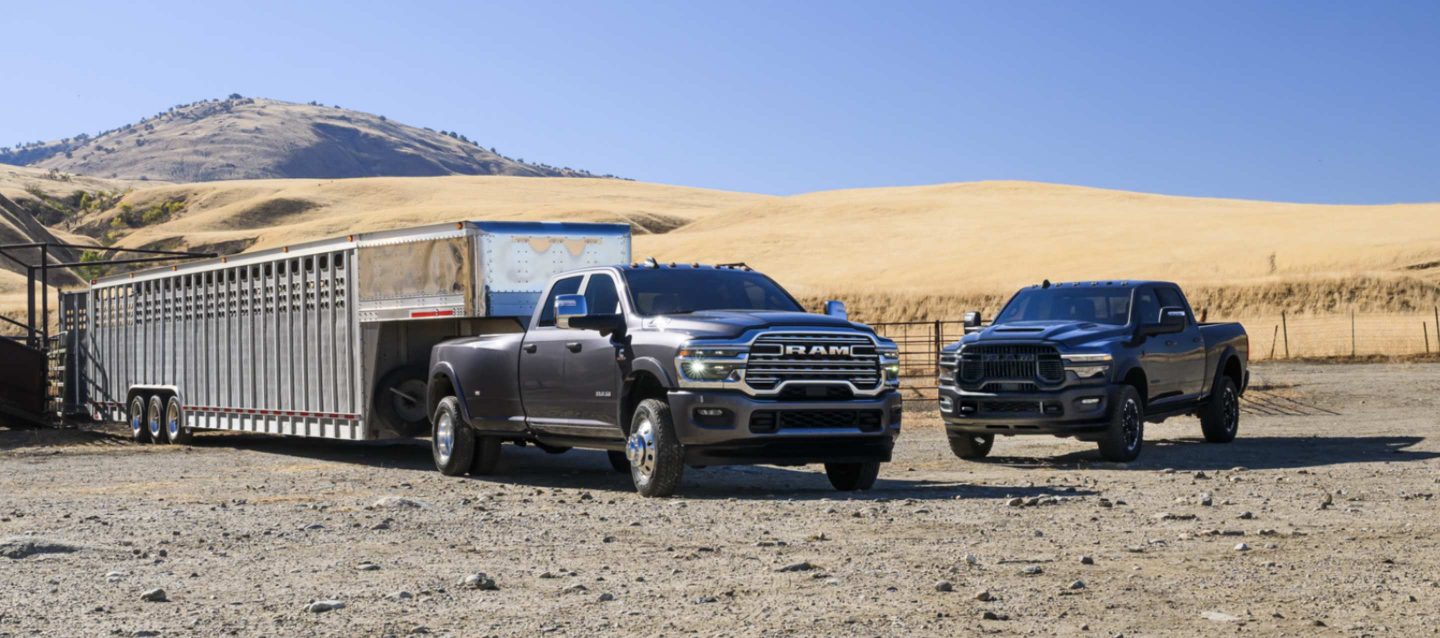 Una Ram 3500 Limited Longhorn 4x4 Crew Cab 2025 acarreando un remolque de quinta rueda grande para ganado y una Ram 2500 Rebel 4x4 Crew Cab negra estacionadas cerca.